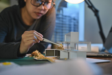Architecture students diligently make house model building samples with paper art architecture tools at night in their alone room.