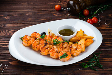 Wall Mural - Fried shrimp on a skewer with rustic potatoes, lemon, tomatoes, olives and sauce, fresh lunch.