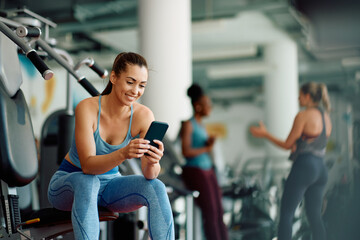 young happy sportswoman using mobile phone while working out in gym.