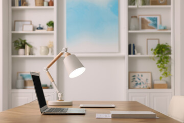 Canvas Print - Interior design. Cosy workplace with laptop and lamp on wooden table near abstract picture between shelves