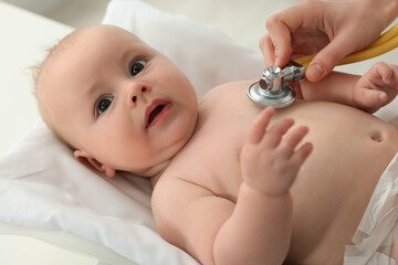 Pediatrician examining cute little baby with stethoscope in clinic, closeup