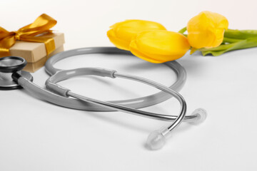 Wall Mural - Stethoscope, gift box and yellow tulips on white background, closeup. Happy Doctor's Day