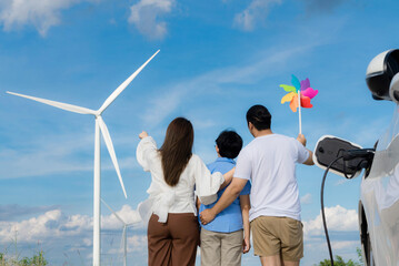 Progressive happy family enjoying their time at wind farm for green energy production concept. Wind turbine generators provide clean renewable energy for eco-friendly purposes.