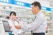 © buritora - 薬局でスマホ決済をする高齢者男性と薬剤師・調剤師の女性