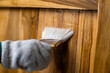 Hand in glove holding brush is applying lacquer or protective varnish on wooden wall. Protect the wood from moisture.