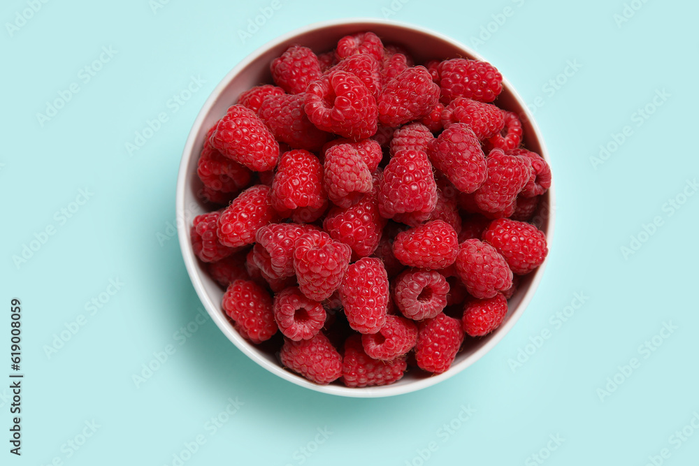 Bowl with fresh raspberries on blue background