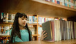 © APchanel - Little girl choosing book in public library room selecting literature for reading. girl chooses books on shelves learning from books is school education benefits of everyday reading concept.