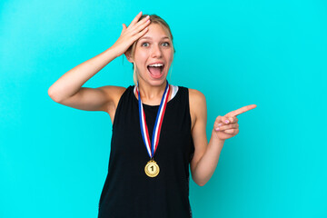 Wall Mural - Young caucasian woman with medals isolated on blue background surprised and pointing finger to the side