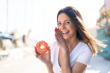 Wall Mural - Young woman at outdoors holding a donut at outdoors whispering something