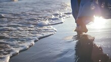 Seaside Serenity: Close-up Of Woman's Skirted Feet Along The Sunset Beach, Waves Washing Away Footprints