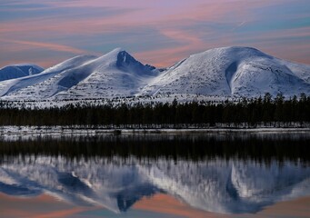 Canvas Print - Snow-capped mountains reflected in the tranquil waters of a lake surrounded by a lush forest.