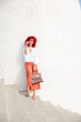 © Renata Hamuda - smiling elegant businesswoman with red afro hair on white stairs holding handbag in hand leaning against white wall talking on smartphone