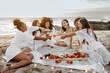 © Prostock-studio - Hen party celebration. Happy diverse women opening bottle of champagne, having picnic on beach at coastline, free space