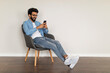© Prostock-studio - Mobile Communication. Indian Guy Messaging On Smartphone, Relaxing In Armchair At Home