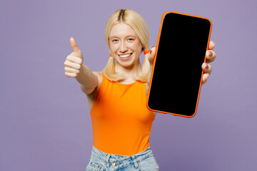 Wall Mural - Young blonde woman wearing orange tank shirt casual clothes hold in hand use close up mobile cell phone with blank screen workspace area show thum up isolated on plain pastel light purple background.