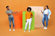 © Prostock-studio - African man and ladies pointing at large bags, orange background