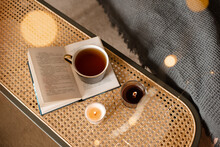 Cup Of Black Tea Stay On Open Paper Book With Scented Candles On Rattan Table In Living Room Top View. Selective Focus. Good Morning.