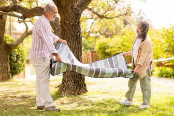 Wall Mural - Happy old european husband and wife put on plaid on grass, enjoy picnic, free time together, nature in park