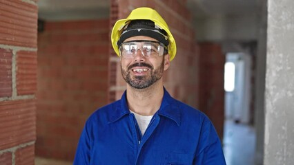 Sticker - Young hispanic man worker wearing hardhat smiling at construction site