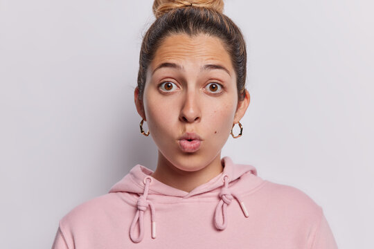 Portrait of amazed young European woman with combed hair holds breath from astonishment reacts to something shocking wears pink sweatshirt isolated over white background. Human reactions concept