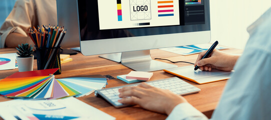 Poster - Graphic designer work on computer laptop and with graphic drawing pen while brainstorming unique design with professional graphic team in modern digital studio workplace. Panorama shot. Scrutinize