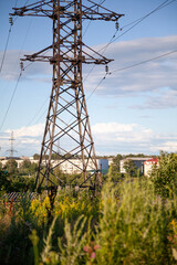 Transmission tower in the green field providing electricity supply for a town. Beautiful landscape with a pylon of a power line in the field among wild plants and grass