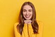 Portrait of cheerful dark haired woman smiles gently keeps hands under chin has sincere positive happy face expression dressed casually poses over vivid yellow background. People and emotions concept