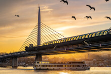 A Ship Passing Under The Bosphorus Bridge At Sunset, Birds Flying Overhead And A Helicopter Flying Over The City.