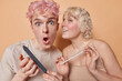 Young woman and man engaging in shared moment of self care use nail file to pamper their nails and do manicure guy with pink hair stares with shocked expression as hears unexpected rumor. Hand care