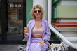 © hurricanehank - Cheerful white woman sitting in a outdoor cafe with a cold brew coffee. Portrait of a stylish female person in purple clothes posing with a disposable brown paper cup in hand