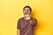 Man pointing and laughing at someone on a yellow studio background.