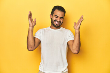 Wall Mural - Casual young Latino man against a vibrant yellow studio background, joyful laughing a lot. Happiness concept.