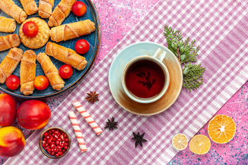 Wall Mural - top view sweet delicious bagels inside tray with plums fresh peaches and cup of tea on light pink desk cake biscuit cookie sweet sugar pie