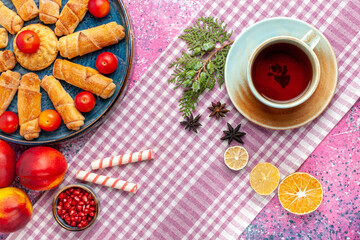 Wall Mural - top view sweet delicious bagels inside tray with plums fresh peaches and cup of tea on light-pink desk cake biscuit cookies sweet sugar pie