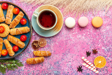 Wall Mural - top view sweet delicious bagels with fresh sour plums french macarons and cup of tea on light pink desk cake biscuit cookie sweet sugar pie