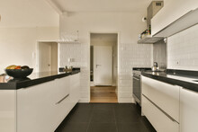 A Kitchen With White Cabinets And Black Counter Tops In The Center Of The Image Is An Open Door Leading To Another Room