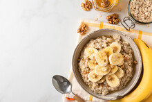 Banana, Walnuts And Honey Oatmeal Porridge In A Bowl With A Spoon On White Table For Healthy Tasty Breakfast. Top View