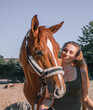 Portrait einer jungen blonden Frau, die neben dem Kopf ihres jungen Pferdes mit Fellhalfter steht und es verliebt anschaut