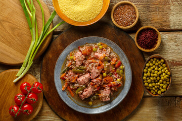 Israeli couscous with sumac and chicken stew pieces on the table in a plate next to spices and vegetables.