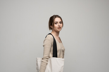 Wall Mural - Cheerful millennial woman with a white eco bag standing over white studio background. Lady holding shopper handbag. Fashion and ecology concept, Selective Focus. No more plastic.