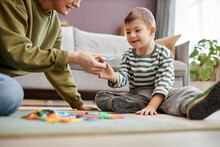 Portrait Of Happy Little Boy With Down Syndrome Playing With Letters On Floor And Enjoying Learning Exercise With Mom