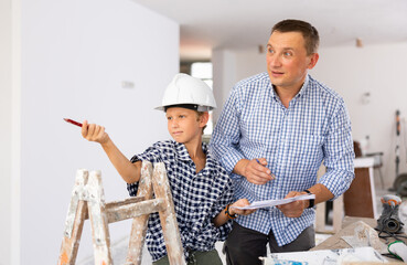 Wall Mural - Father and his young son discussing work plan in construction site in apartment, making pointing finger gesture.