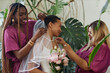 © Seventyfour - Side view portrait of two bridesmaids helping young black bride getting ready for wedding ceremony