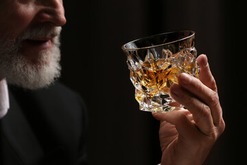 Man holding glass of whiskey with ice cubes on dark background, closeup