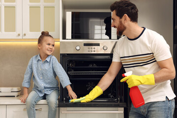 Wall Mural - Spring cleaning. Father and daughter tidying up oven in kitchen together