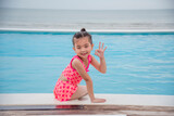 Fototapeta Pomosty - Toddler girl Kid swim playful in swimming pool summer time with pink swimwear in blue water at hotel swimming pool outdoor. Happy girl swim playful water splash with happiness on summer vacation
