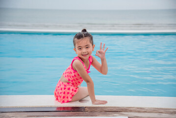 Toddler girl Kid swim playful in swimming pool summer time with pink swimwear in blue water at hotel swimming pool outdoor. Happy girl swim playful water splash with happiness on summer vacation