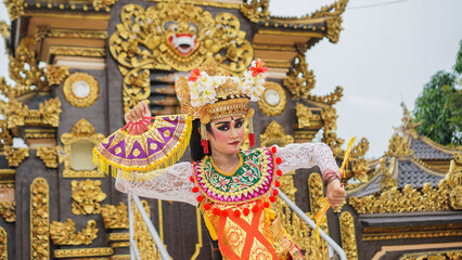 Canvas Print - girl wearing Balinese traditional dress with a dancing gesture on Balinese temple background with hand-held fan, crown, jewelry, and gold ornament accessories. Balinese dancer woman portrait
