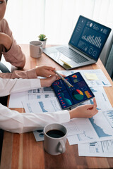 Analyst team colleague discuss financial data on digital dashboard, analyzing charts graph display on laptop and tablet screen. Modern office use business intelligence to plan marketing. Enthusiastic