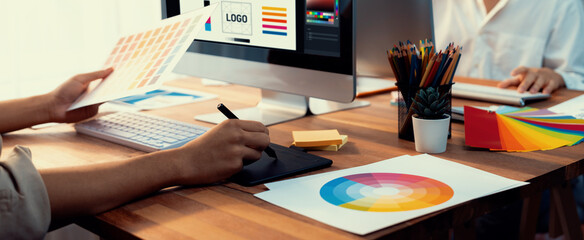 Poster - Graphic designer work on computer laptop and with graphic drawing pen while brainstorming unique design with professional graphic team in modern digital studio workplace. Panorama shot. Scrutinize